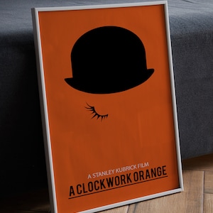 Puede incluir: Un p&oacute;ster enmarcado con fondo naranja y una silueta negra de un bomb&iacute;n con una pesta&ntilde;a. El texto "A STANLEY KUBRICK FILM A CLOCKWORK ORANGE" est&aacute; impreso en negro en la parte inferior del p&oacute;ster.