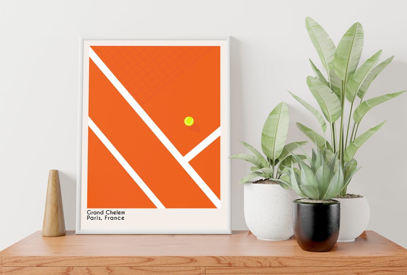 May include: A minimalist poster with a graphic design of a tennis court in orange with white lines and a yellow tennis ball. The text "Grand Chelem Paris, France" is at the bottom of the poster.
