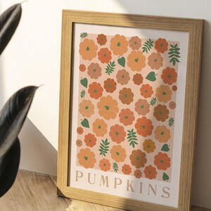 May include: A framed print featuring a pattern of orange and brown pumpkins on a pale pink background. The print has the word "PUMPKINS" at the bottom.