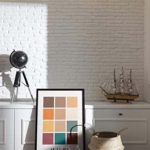 May include: A framed print with a color palette of autumnal colors, including orange, yellow, brown, red, and green. The print is titled "AUTUMN" and is displayed on a white shelf with a globe and a model sailboat.