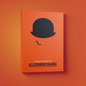 Puede incluir: Un p&oacute;ster minimalista con fondo naranja que presenta un sombrero bomb&iacute;n negro y un ojo con una sola pesta&ntilde;a. El texto "A Stanley Kubrick Film A Clockwork Orange" est&aacute; impreso en negro en la parte inferior.