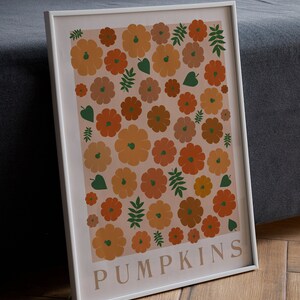 May include: A framed print featuring a pattern of orange, brown and green pumpkins and leaves on a pale pink background. The print has the word "PUMPKINS" in white text at the bottom.