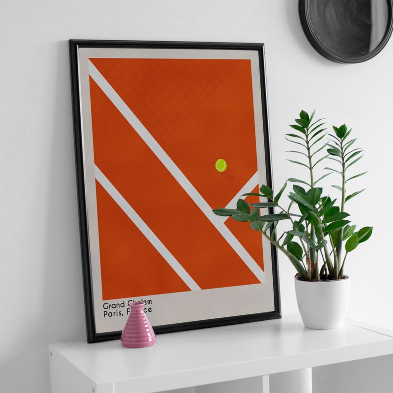 May include: A framed poster with a minimalist design of a tennis court in orange and white with a yellow tennis ball. The poster has the text "Grand Chelem Paris, France" at the bottom.