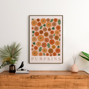 May include: A digital print featuring a pattern of orange and brown pumpkins with green leaves on a pale pink background. The print has the word "PUMPKINS" at the bottom.