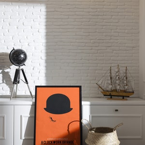 Puede incluir: Un p&oacute;ster en blanco y negro con fondo naranja que presenta la silueta de una persona con un sombrero de copa y el texto "A Stanley Kubrick Film: A Clockwork Orange".