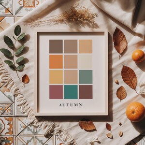 May include: A framed print with a color palette of 12 squares in shades of brown, orange, yellow, green, and purple. The squares are arranged in a grid pattern. The word "AUTUMN" is printed below the grid.