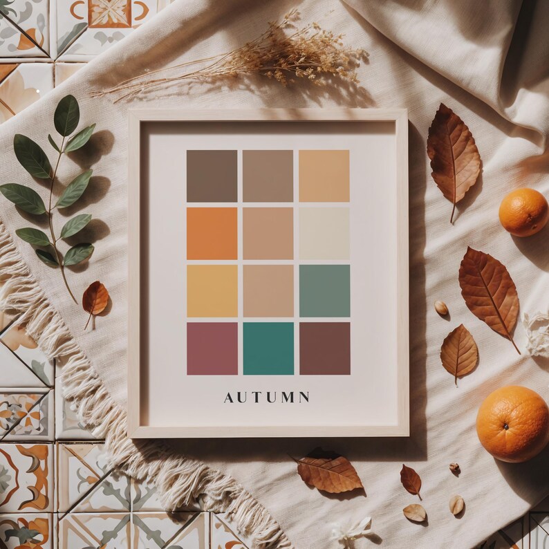 May include: A framed print with a color palette of 12 squares in shades of brown, orange, yellow, green, and purple. The squares are arranged in a grid pattern. The word "AUTUMN" is printed below the grid.