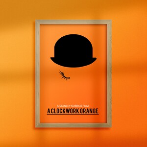 Puede incluir: Un p&oacute;ster minimalista con una silueta negra de un bomb&iacute;n y un ojo con una pesta&ntilde;a. El p&oacute;ster tiene un fondo naranja brillante y un marco de madera. El texto "A Stanley Kubrick Film A Clockwork Orange" est&aacute; impreso en negro en la parte inferior del p&oacute;ster.