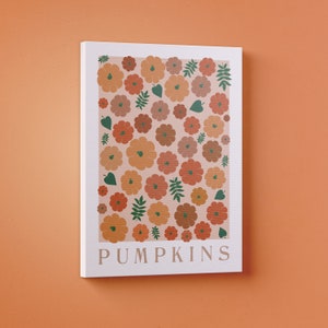 May include: A white canvas print featuring a pattern of orange, brown, and green pumpkins on a pale pink background. The text "PUMPKINS" is printed in green at the bottom of the print.