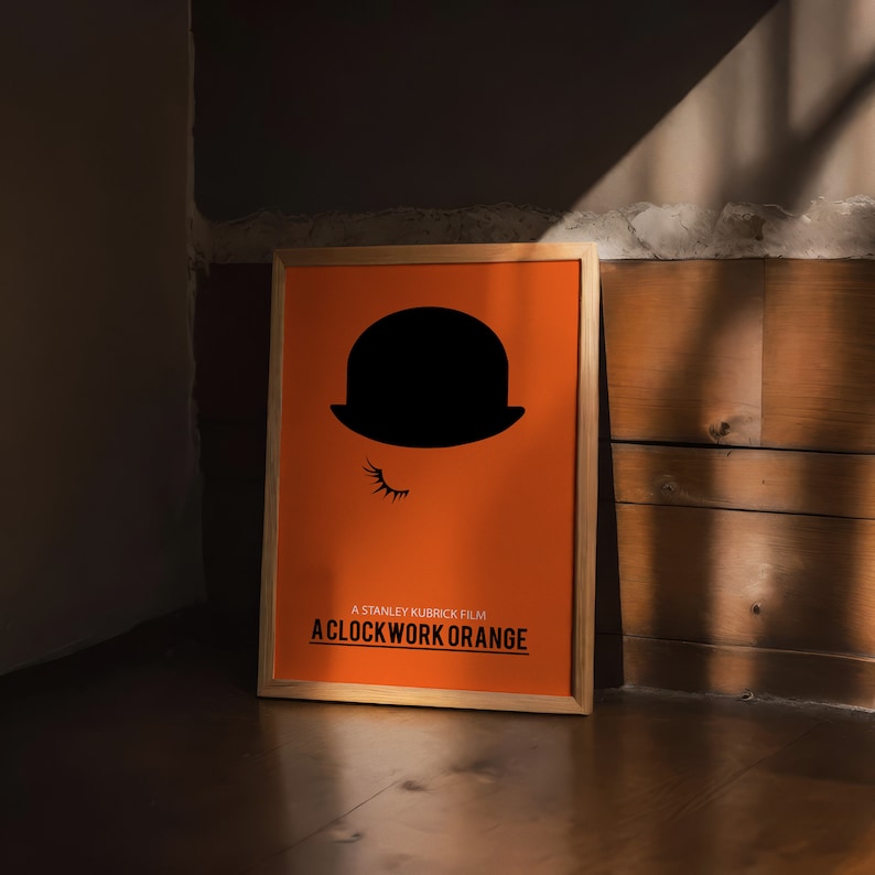 Puede incluir: Un p&oacute;ster enmarcado con fondo naranja y una silueta negra de un bomb&iacute;n con un ojo. El texto "A Stanley Kubrick Film A Clockwork Orange" est&aacute; impreso en negro en la parte inferior del p&oacute;ster.
