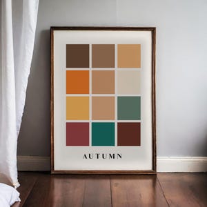 May include: A framed print with a color palette of 12 squares in shades of brown, orange, yellow, green, and red. The word "AUTUMN" is printed in black at the bottom of the print.