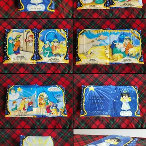 Pode incluir: Um livro de tecido azul e amarelo com ilustra&ccedil;&otilde;es da hist&oacute;ria da natividade. O livro &eacute; intitulado "Little Light" por Joy Allen. O livro est&aacute; aberto na p&aacute;gina que diz "Little Light, born this starry night."