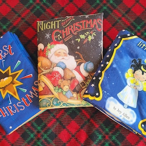 Pode incluir: Tr&ecirc;s livros de cart&atilde;o azul com temas natalinos. O primeiro livro &eacute; intitulado "The First Christmas" e apresenta uma estrela amarela com um pres&eacute;pio dentro. O segundo livro &eacute; intitulado "Night Before Christmas" e apresenta o Papai Noel em um tren&oacute; com um urso de pel&uacute;cia. O terceiro livro &eacute; intitulado "Little Light" e apresenta um anjo com uma aur&eacute;ola e uma vela.