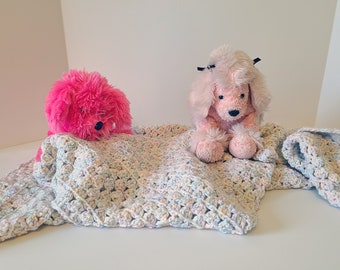 Pode incluir: Dois cães de pelúcia rosa, um com um laço preto, estão deitados em um cobertor de crochê multicolorido.