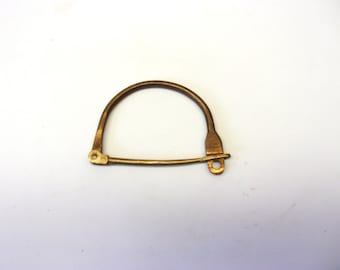 Puede incluir: Un cierre de metal de tono latón vintage, con una parte superior curvada y una barra inferior recta. El cierre tiene un diseño articulado con un pequeño lazo en un extremo para la fijación. El metal tiene un aspecto ligeramente envejecido.