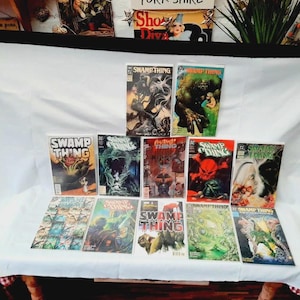 Könnte beinhalten: Eine Sammlung von Swamp Thing-Comics mit verschiedenen Covern, die den Swamp Thing-Charakter zeigen. Die Comics sind auf einer weißen Oberfläche angeordnet und präsentieren die lebendigen Farben und Illustrationen der Serie.