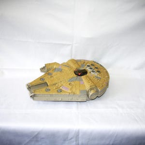 May include: A detailed model of the Millennium Falcon starship, in tan and grey with red and purple details. This replica of the iconic ship from the Star Wars franchise is highly detailed.