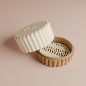 Op de afbeelding: Een witte en bruine plastic container met een golvend ontwerp aan de binnenkant. De container heeft een deksel met een reliëf.