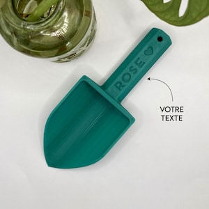 Peut inclure: Une petite pelle de jardin en vert sarcelle avec un manche sur lequel est inscrit "ROSE" avec un symbole de cœur.