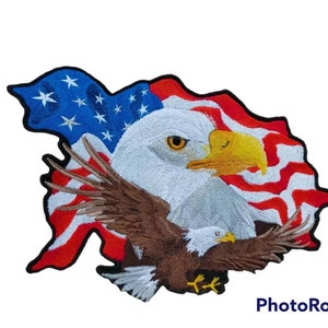 Peut inclure: Un patch brodé représentant un aigle chauve avec les ailes déployées, perché sur un drapeau américain flottant. La tête de l'aigle est tournée vers la droite, avec un regard vif et concentré. Le drapeau est rouge, blanc et bleu, avec des étoiles dans le champ bleu.