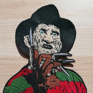 Peut inclure: Patch brodé représentant Freddy Krueger de la franchise de films Nightmare on Elm Street. Il porte un pull rayé rouge et vert et un chapeau noir. Il a une expression menaçante avec des yeux verts et un gant tranchant avec des lames.