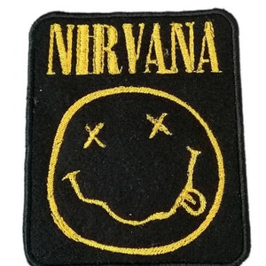 Peut inclure: Patch brodé noir et jaune avec le mot "NIRVANA" en lettres jaunes au-dessus d'un smiley jaune avec deux X pour les yeux.