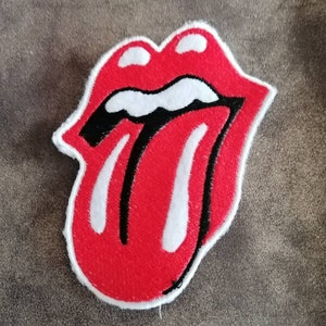 Könnte beinhalten: Roter gestickter Aufnäher mit weißem Rand, der eine Zunge zeigt, die aus einem Mund herausragt. Die Zunge ist schwarz mit weißen Streifen und der Mund ist rot.