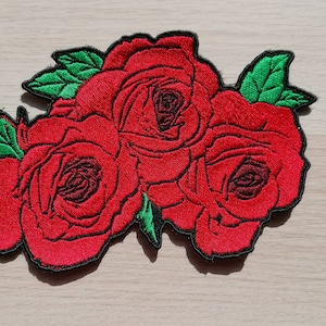 Peut inclure: Un patch brodé représentant trois roses rouges avec des feuilles vertes. Les roses sont disposées en grappe et présentent un design détaillé.