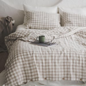 May include: A white and brown gingham bedding set with a green mug and a book on top of the bed.