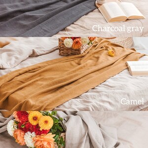 K&ouml;nnte beinhalten: Drei Bettw&auml;sche-Sets aus Leinen in verschiedenen Farben: Anthrazitgrau, Kamel und Natur. Die Sets sind auf einem Bett mit einem Blumenstrau&szlig; in einem Weidenkorb drapiert.