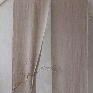 May include: A pair of beige linen curtains hanging from a white rod. The curtains are open in the middle, revealing a white wall behind them. A dried branch in a clear glass vase sits in front of the curtains.