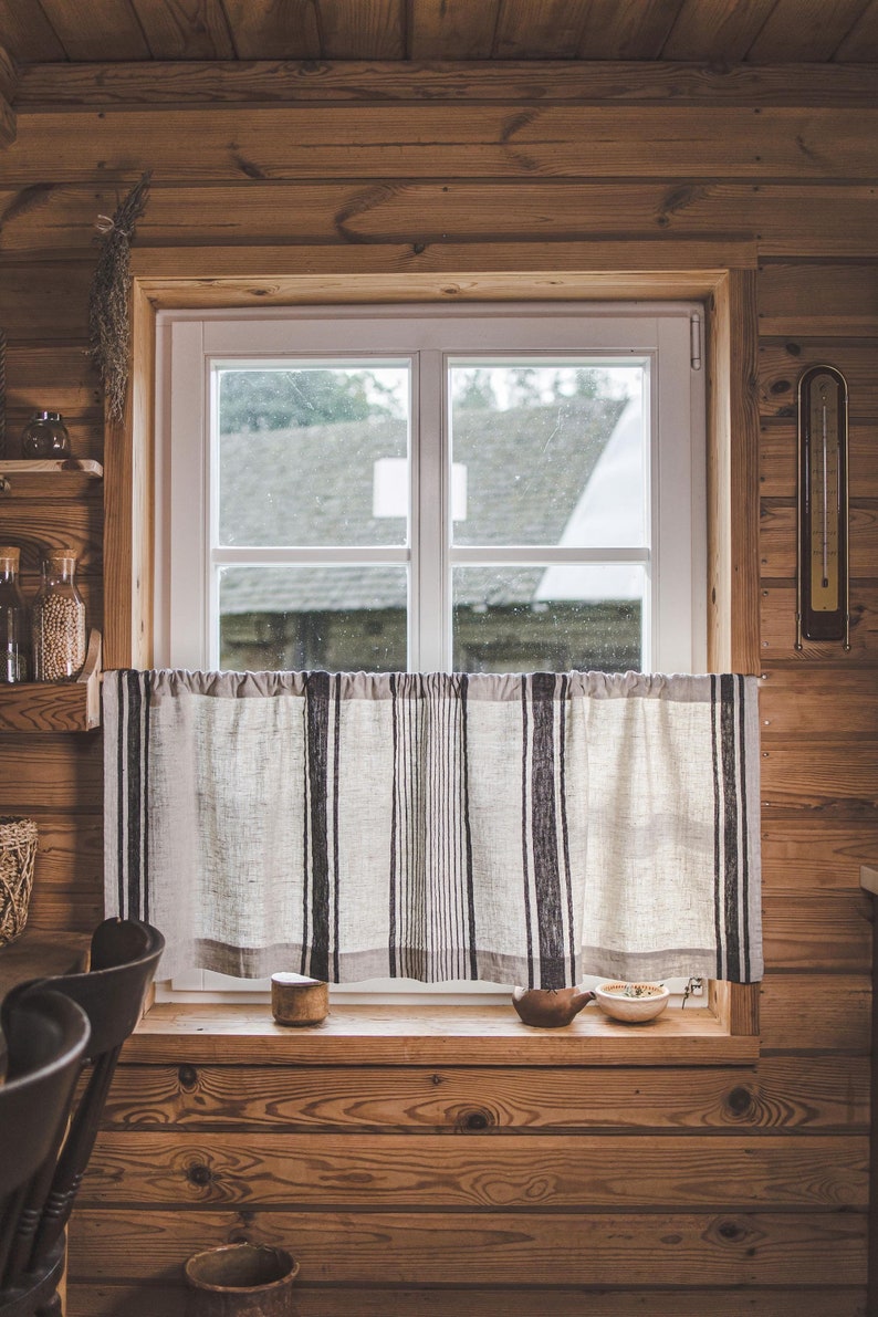 May include: A window with a white frame and a view of a building through the glass. The window is covered with a white and black striped curtain.