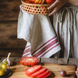 Puede incluir: Una persona sosteniendo una cesta tejida llena de tomates rojos y naranjas. Una tabla de cortar de madera con tomates en rodajas y otras verduras est&aacute; sobre una mesa de madera.