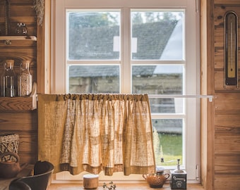 Könnte beinhalten: Rustikale Küchenszene mit einem Fenster mit beigefarbenem Vorhang. Auf der Fensterbank stehen eine kleine Keramiktasse, eine dekorative Teekanne und eine alte Kaffeemühle. Die Wände sind mit warm getäfeltem Holz verkleidet.