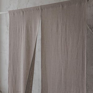 May include: A pair of light brown linen curtains hanging from a white rod. The curtains are made of a textured fabric and have a natural, rustic look.