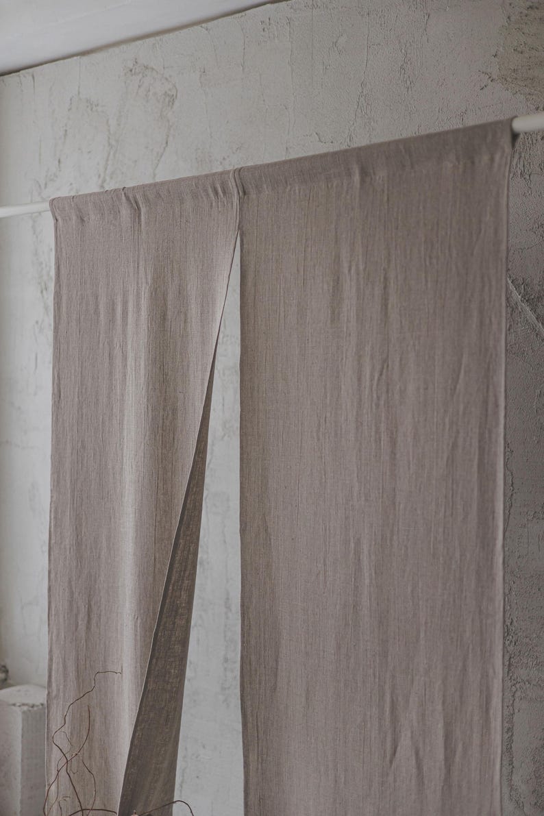 May include: A pair of light brown linen curtains hanging from a white rod. The curtains are made of a textured fabric and have a natural, rustic look.