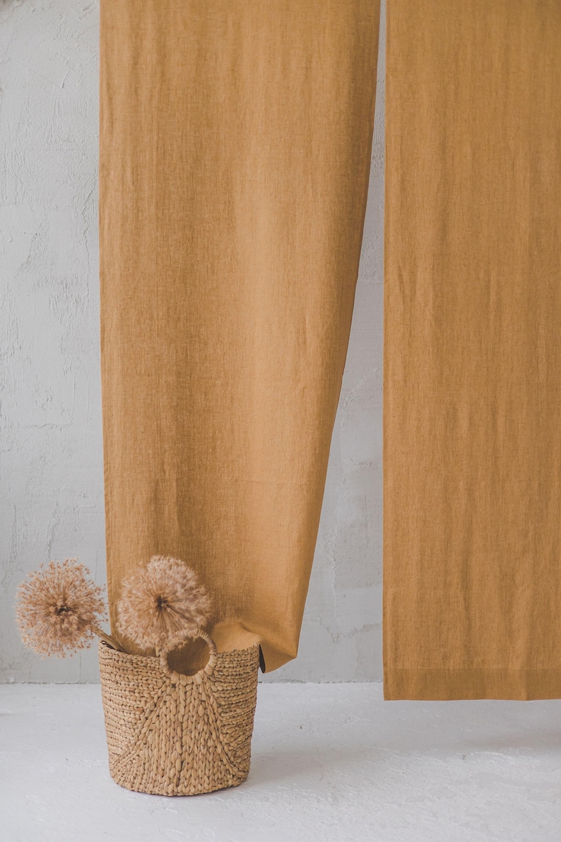May include: A woven basket with a handle sits in front of a pair of mustard yellow linen curtains.