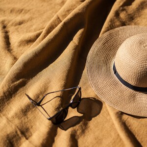 May include: A straw hat and sunglasses on a brown linen fabric background.