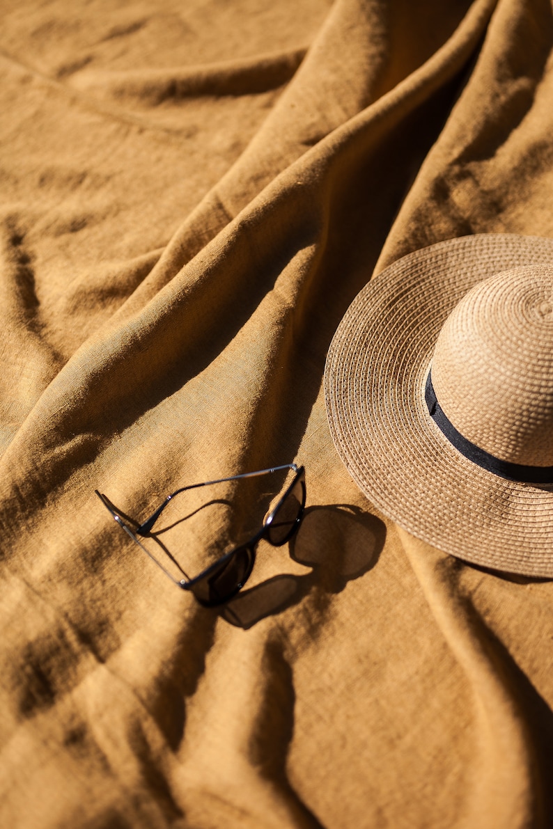 May include: A straw hat and sunglasses on a brown linen fabric background.
