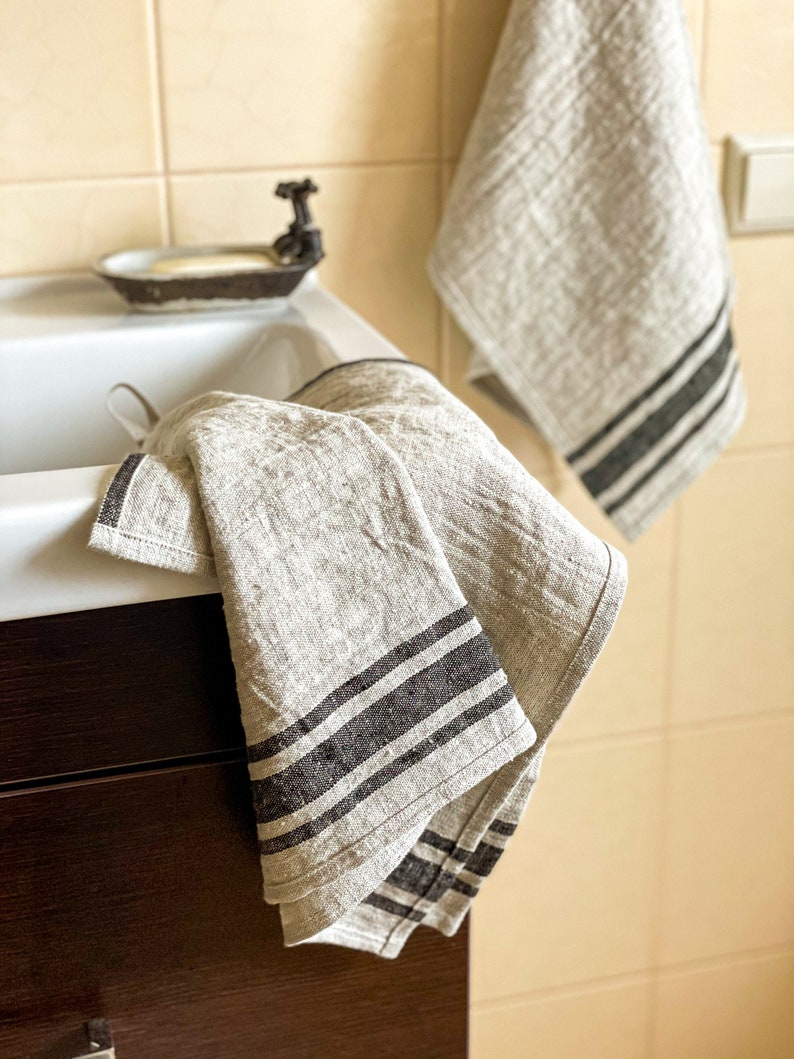 Puede incluir: Dos toallas de cocina de lino grises con rayas negras colgadas en un ba&ntilde;o. Las toallas est&aacute;n dobladas y colgadas sobre un armario.
