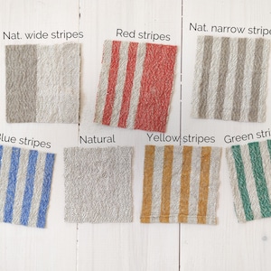 May include: A collection of fabric swatches in various colours and patterns, including natural, red, blue, yellow, and green stripes. The swatches are arranged in rows on a white wooden surface.