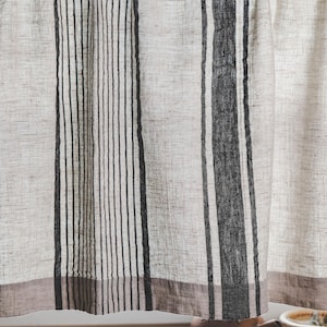 May include: A pair of white and black striped linen curtains with a brown trim. The curtains are hanging in a window and are pulled to the side.