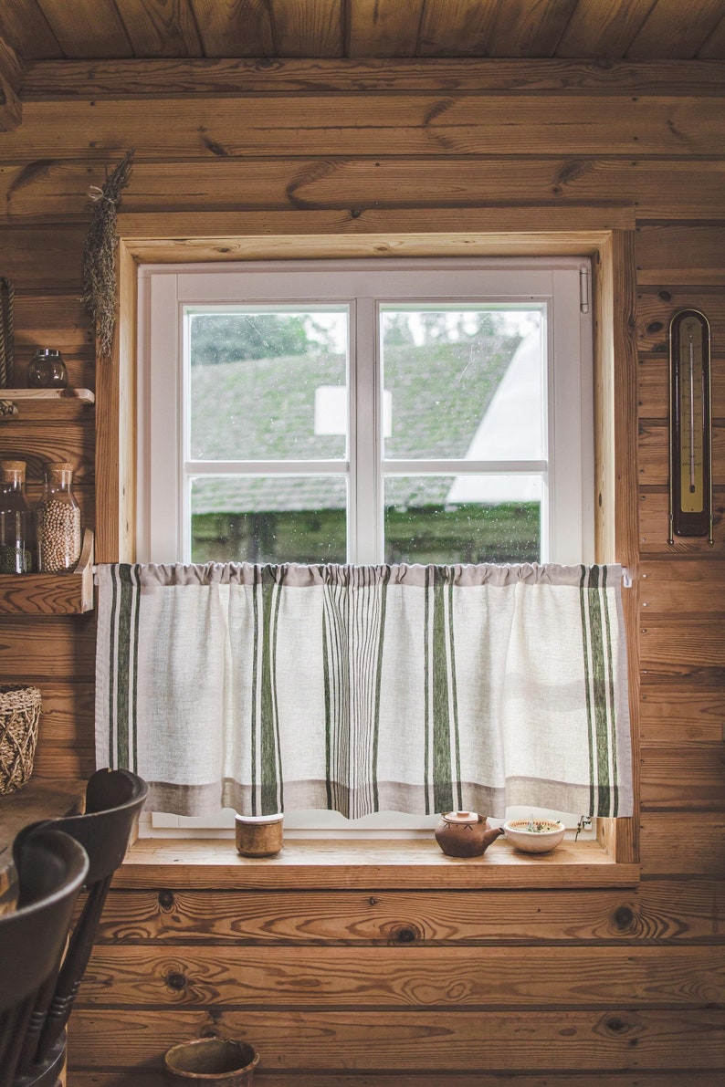 May include: A window with a white frame and a view of a green field. The window is covered with a white and green striped curtain. There are two small ceramic pots on the windowsill.