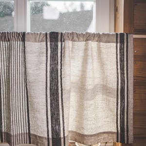 May include: A window with a white frame and a view of a cloudy sky. A white linen curtain with black stripes hangs in front of the window. A small brown teapot and a white bowl with green leaves are on the windowsill.