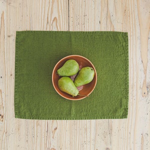 May include: Three green pears in a brown bowl on a green placemat on a wooden surface.