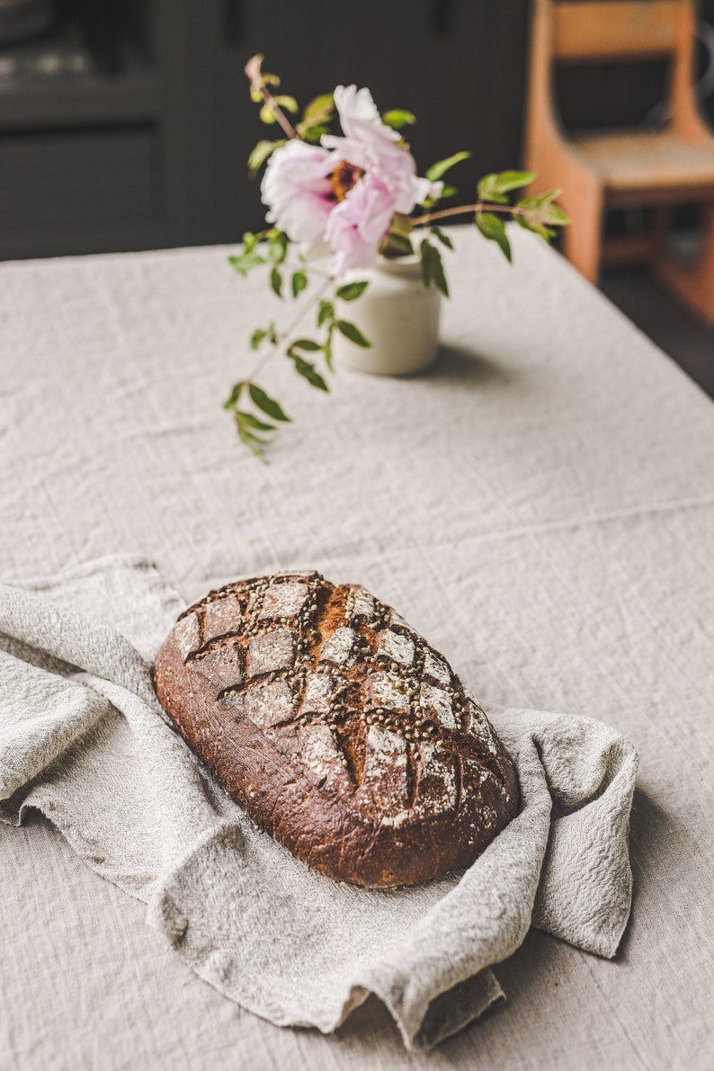 May include: A loaf of crusty bread with a diamond pattern on top, sitting on a linen napkin on a light grey table.