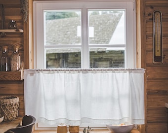 May include: A white cafe curtain hangs on a rod across the lower half of a window set into a wooden wall. The curtain is made of a plain, light-colored fabric with a simple hem at the bottom, partially obscuring the view of the outdoors.