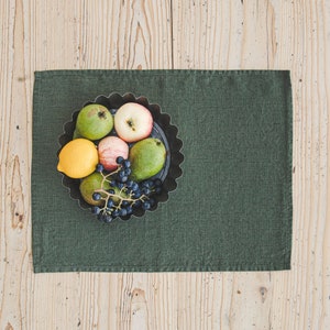 Puede incluir: Un mantel individual de lino verde con un cuenco de metal lleno de fruta. El cuenco contiene un limón, dos manzanas, dos peras y un racimo de uvas.