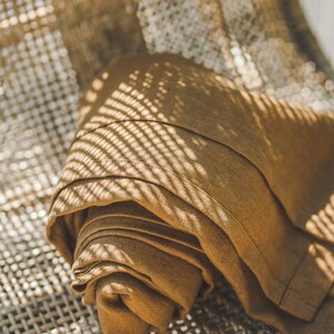 May include: A brown linen throw blanket folded and placed on a woven wicker chair. The blanket is textured and has a subtle sheen. The chair is made of natural materials and has a rustic look.