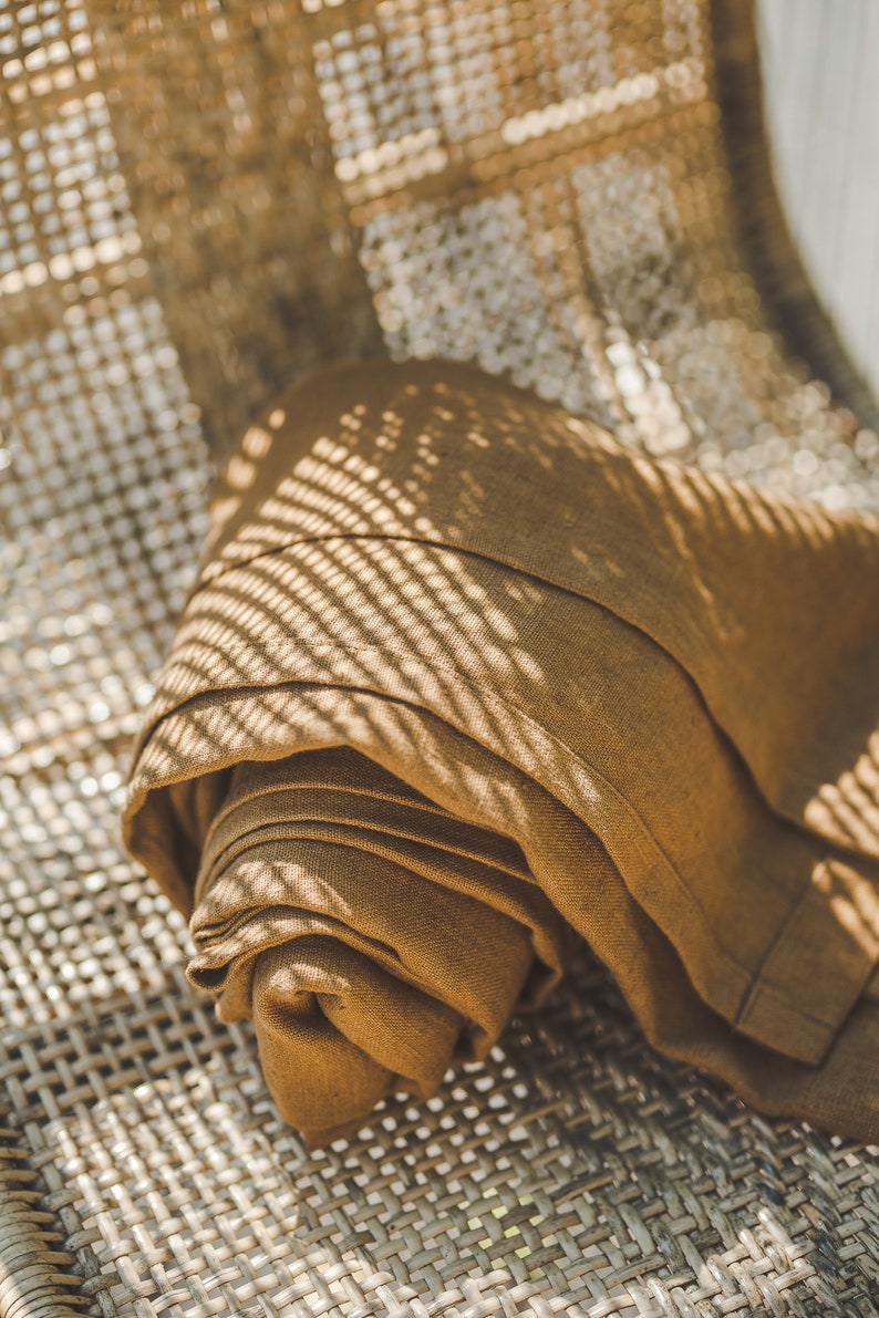 May include: A brown linen throw blanket folded and placed on a woven wicker chair. The blanket is textured and has a subtle sheen. The chair is made of natural materials and has a rustic look.